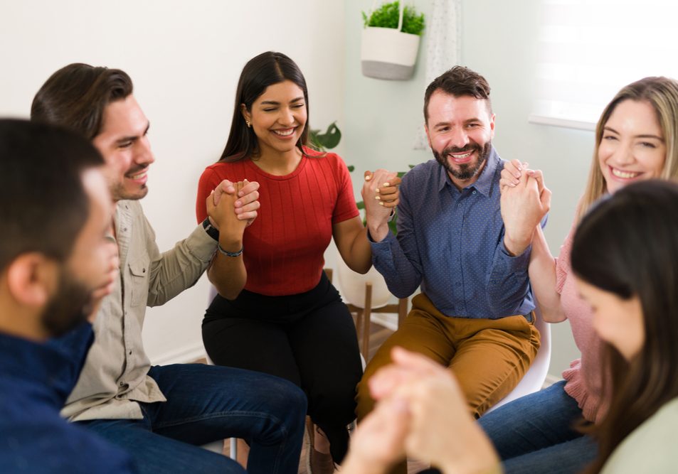 Celebrating the arrival of a new member Happy members of a rehab group laughing while holding hands. Cheerful and excited young men and women in a support group